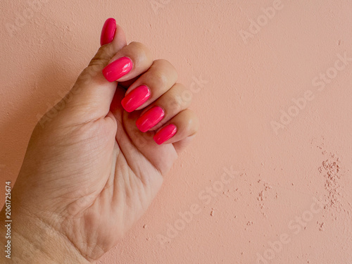 Close-up feemale hand with pink gel polished manicure on peach background,photo