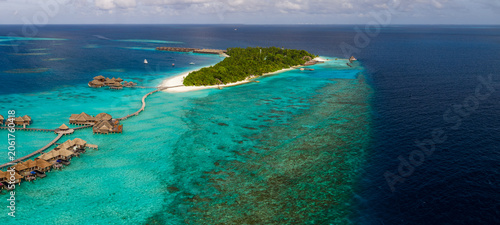 Foto Aerial view of a Maldives luxury resort shows palm island, bright white sand, turquoise shallows, and deep ocean, with curving walkways, water villas, and coral reefs