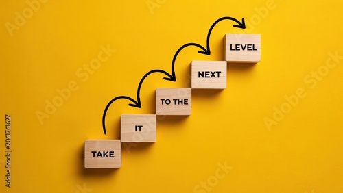 Wooden blocks with text take it to the next level arranged in stairs on yellow background