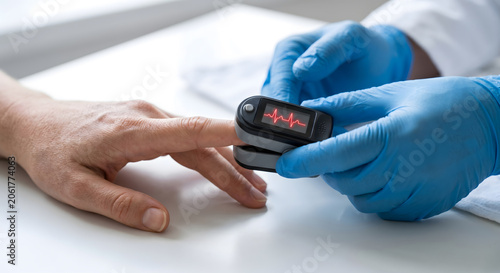 Doctor wearing blue gloves uses pulse oximeter on patient finger monitoring heart rate and oxygen saturation.