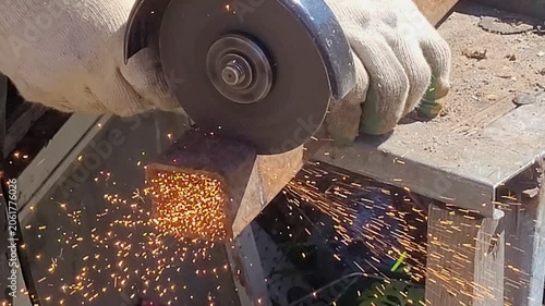 Male hand cuts off pieces of pipe with angle grinder. Cutting of a steel with splashes of sparks at construction site. Sparks during cutting of metal angle grinder