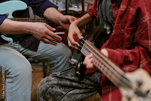Obraz na płótnie Close up of teenager learning bass guitar with adult instructor guiding hand pla