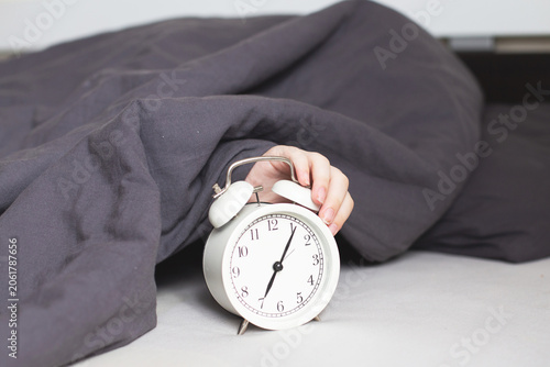 Sleeping person lying on the bed in bedroom and stopping alarm clock