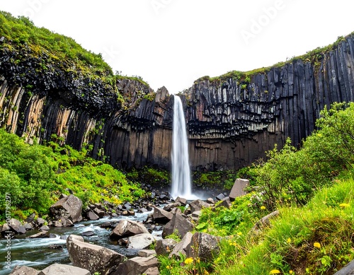 A serene waterfall cascades down a rugged cliffside surrounded by lush greenery and unique rock formations