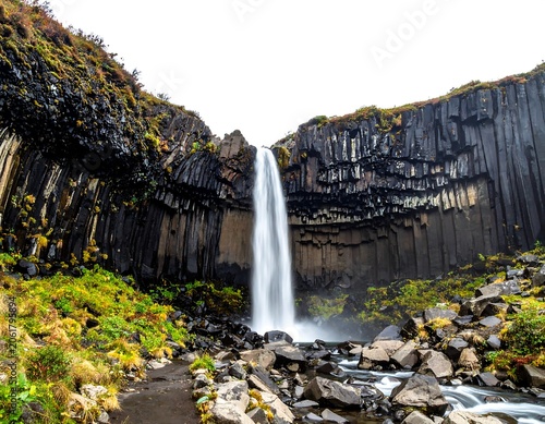 A serene waterfall cascades down a rugged, moss-covered cliffside surrounded by rocks and greenery