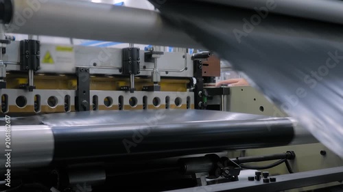 Automatic plastic bag making machine: perforating press unit - production of packaging black garbage bags at plant, factory: close up. Industry, equipment, manufacturing, and recycling concept