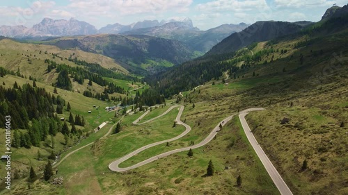 Curving mountain road crossing an alpine valley with forests and distant rocky peaks
