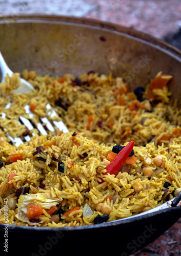 Foto Cooking traditional uzbek pilaf in a large wok kazan with red chili pepper and m
