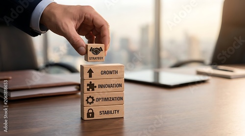 Hand placing a wooden block labeled strategy with a handshake on a stack of business concepts in an office setting