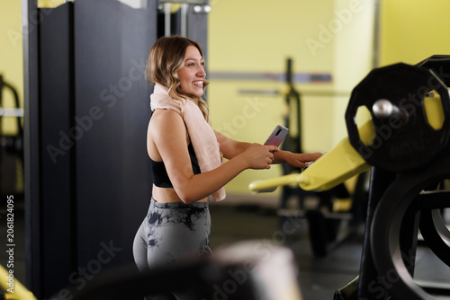Bild auf Leinwand Woman smiles while using her phone and resting in a gym setting during a workout
