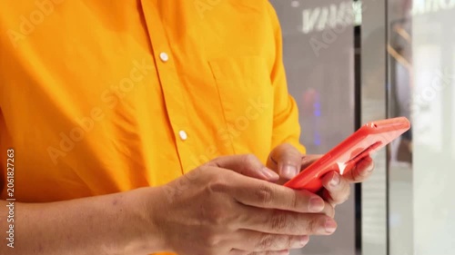 Close Up of Man in Orange Shirt Using Red Smartphone to Text and Browse