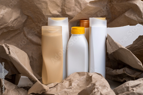 Collection of assorted empty plastic cosmetic bottles arranged on crumpled brown kraft paper, recycling concept