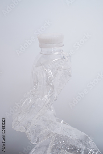 Single crushed clear plastic bottle on a clean white surface, plastic waste and recycling concept
