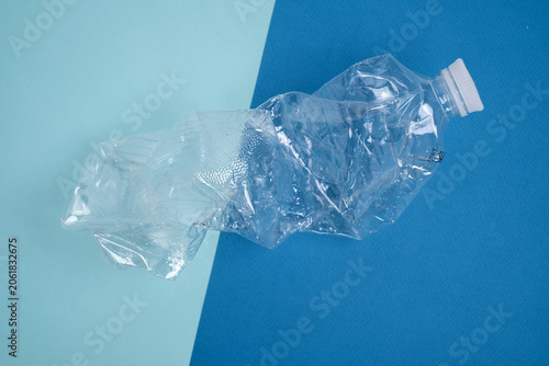 Crushed clear plastic bottle on a split light blue and dark blue background, plastic waste and recycling concept