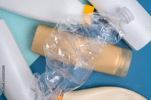 Crushed plastic bottle on top of assorted cosmetic containers, plastic waste and recycling concept