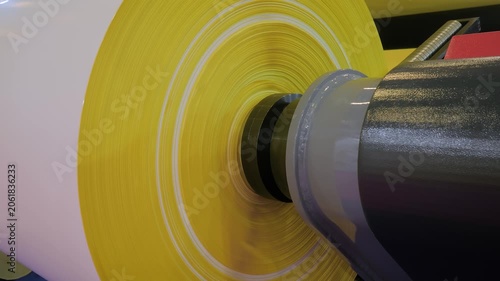 Feed roll with multilayer plastic film - part of automatic plastic bag making machine at packaging exhibition, factory: close up. Manufacturing, recycling, production and technology equipment concept