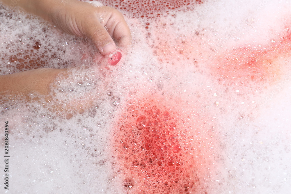 Fototapeta premium Child holding a small pink toy in a bubble bath close-up.