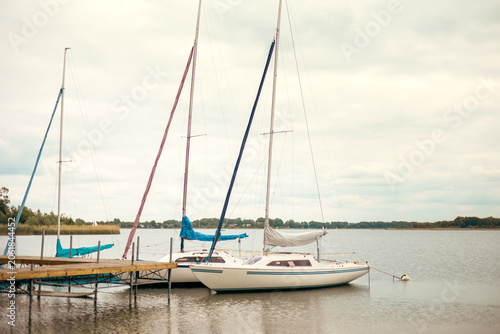 Sailing yachts with lowered sails moored beside a pier on a peaceful lake