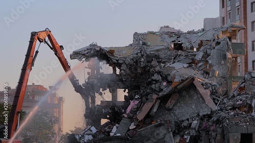 Excavator with hydraulic crusher is tearing down the old typical Turkish multi-storey apartment, residential building in Istanbul, Turkey. Water dust control during demolition of building, slow motion