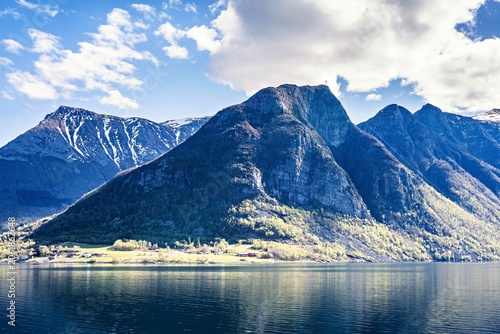 Mountains reflect in water while clouds hover above in Norway during sunny daylight
