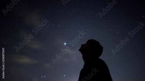 Man silhouetted looking up at bright star in clear night sky over rural landscape