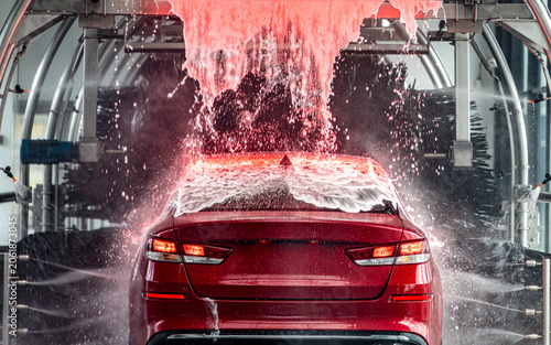 Red car in red foam in automatic tunnel car wash. 
