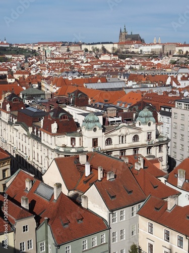 Aerial view of Prague: historic buildings with tiled roofs, Prague Castle, and city skyline on a clear sunny day. Landmarks and historic architecture of Prague, Czech Republic.