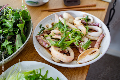 Freshly prepared sliced squid served with spring onions and a savory soy-based sauce on a dining table at home. This simple seafood dish highlights tender squid, aromatic green onions, and rich umami 