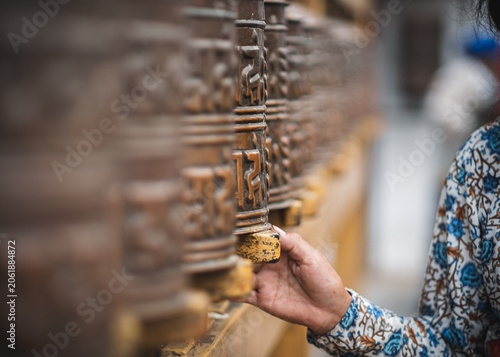 Female and reverently turns a row of decorative metal prayer wheels at a sacred site in Kathmandu Nepal