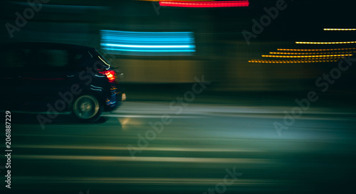 Φωτογραφία Dark car drives quickly along a city road at night, creating light trails and mo