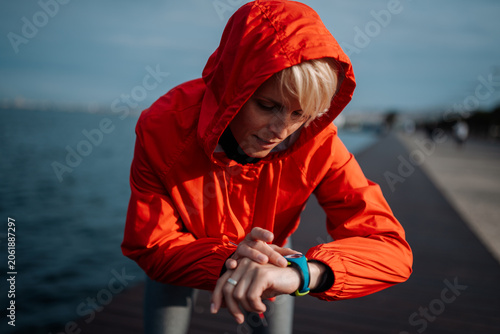 Foto Fit woman setting smartwatch before running on seaside promenade.