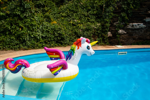 Unicorn pool float in blue water background, inflatable swim tube. Pool party, summer holidays, beach vacation. Fantasy swim ring for summer pool trip. Copyplace, place for text