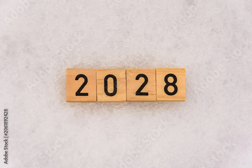 The number 2028 is made of wooden blocks on a snowy background. Textured background with snow. New Year's concept.