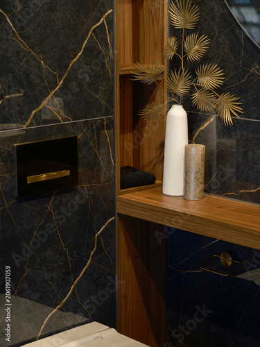 Canvastavla Detail of a dark veined marble bathroom with a gold flush plate, a wood shelf niche with a vase and candle and a blue stone cabinet