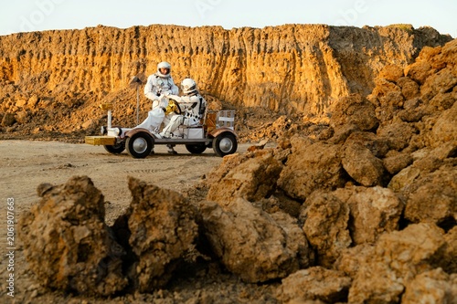 Exploration on Mars with astronauts driving a rover near rocky terrain at sunset