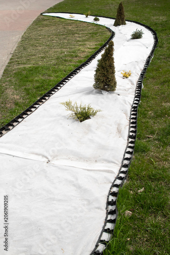 Curved garden path with ornamental plants and white landscaping mesh without gravel