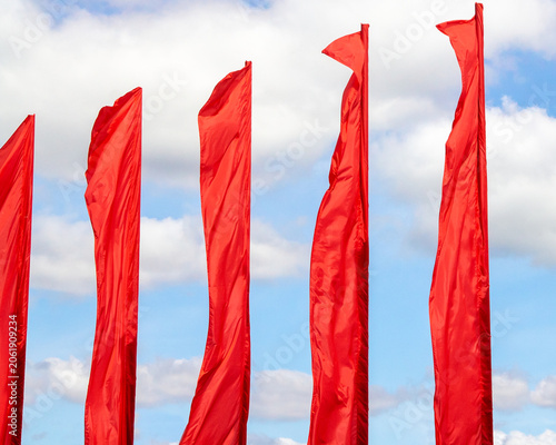 Red fabric flags waving against a blue sky with white clouds