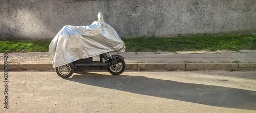 Scooter covered with silver protective cover parked on city street
