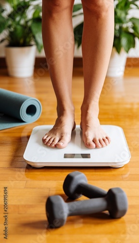 Woman Standing on Digital Weight Scale at Home with Fitness Equipment