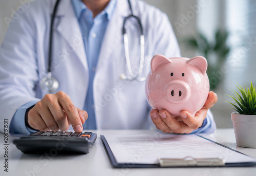 Doctor holding piggy bank using calculator for medical cost and health insurance