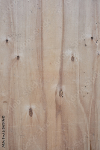 Detailed close-up texture of weathered plywood with deep vertical cracks and unique organic grain patterns. The brown wooden board backdrop features rustic rough fibers 