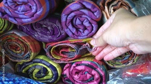 Close up of person choosing colorful woven loincloth fabric rolls in local shop.