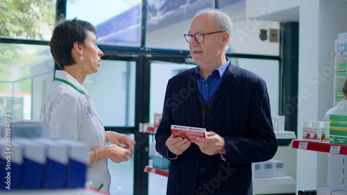 Quadro em tela Aged man in chemist store asking pharmacist for medical opinion, needing treatme