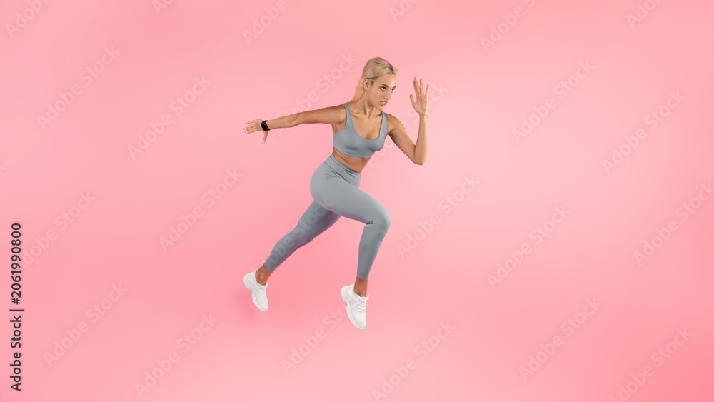 Naklejka premium Focused Young Athletic Caucasian Woman Running In Sportswear, Captured In Action Pose Against Pink Background. Promoting Fitness And Active Lifestyle In Gym Or Outdoor Setting, Energy And Motion.