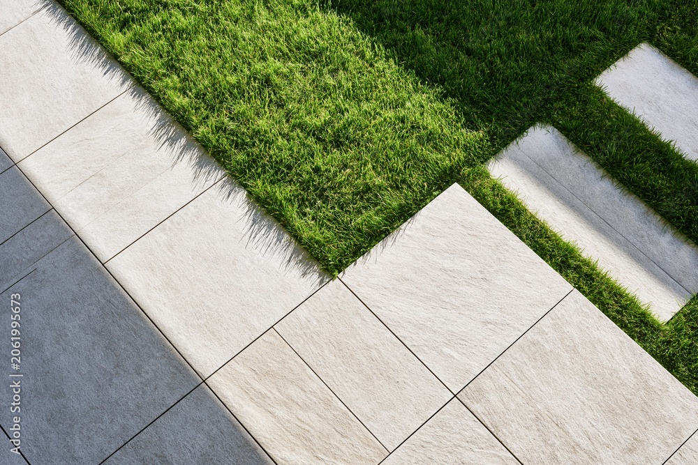 Fototapeta premium Patch of green lawn on modern tiled patio walkway corner