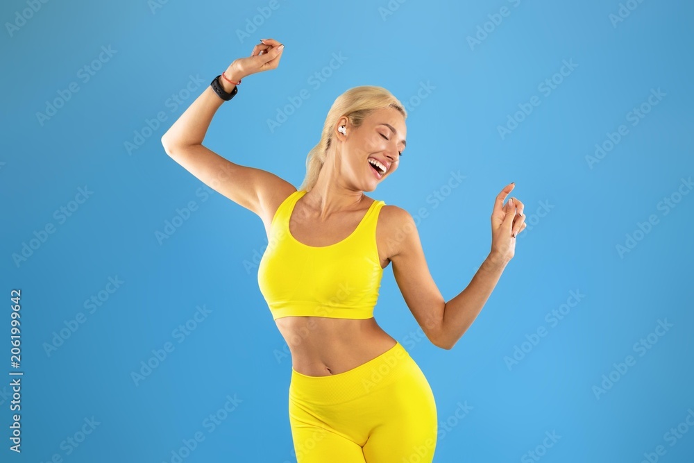 Naklejka premium Smiling Young Woman In Yellow Activewear Dancing With Joy In Fitness Studio, Expressing Happiness And Energy While Enjoying Workout, Indoor Environment. Weight Loss Concept.