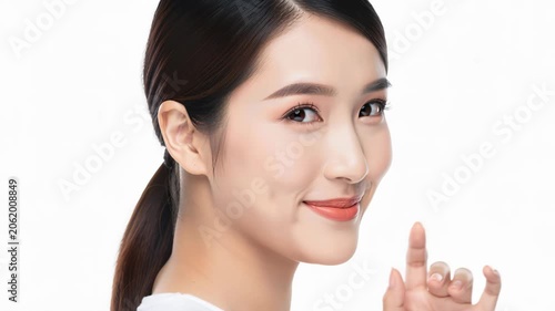 Asian Woman with Dimple Smile: A beautiful Asian woman with a charming dimple smiles gently while touching her chin, showcasing her natural beauty.