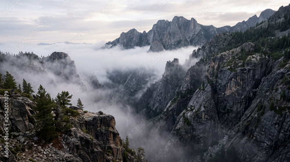 Obraz premium Deep mountain ravine is enveloped in thick morning fog showing jagged granite cliffs landscape view.