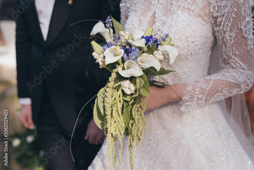 Close up of bride in elegant lace wedding dress holding a luxury calla lily bouquet
