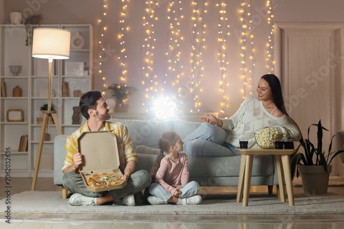 Family with tasty snacks watching movie together at home